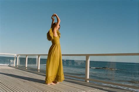 A Woman In A Yellow Dress Is Standing On A Pier Near The Ocean And