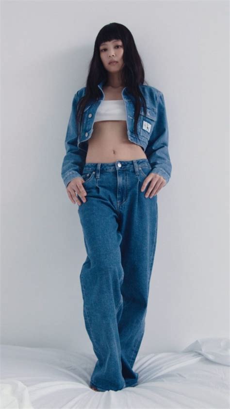 A Woman Standing In Front Of A White Wall Wearing Blue Jeans And A Crop Top