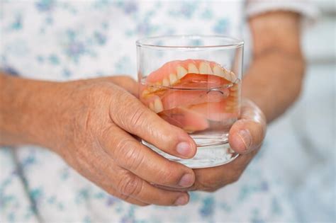 Paciente idosa asiática segurando e lavando dentadura em vidro de