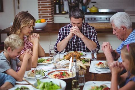 Família de várias gerações orando os avós sentado à mesa de