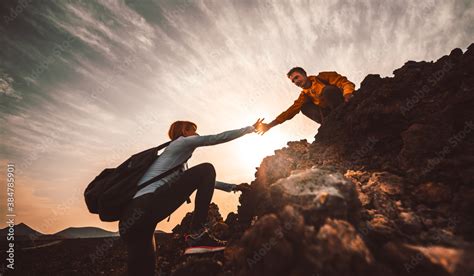 Couple Of Hikers Helping Each Other Climbing A Mountain At Sunset