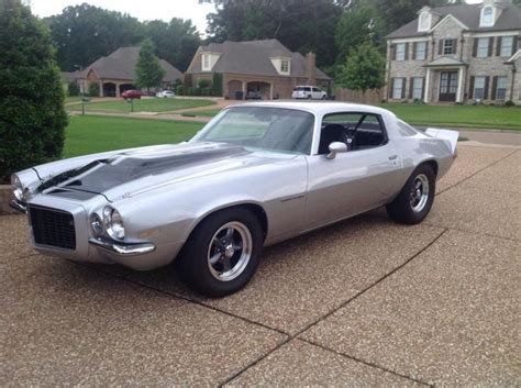 a silver muscle car parked in front of a house