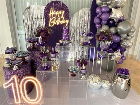 A Table With Purple And Silver Decorations Balloons And Cake On It S Side