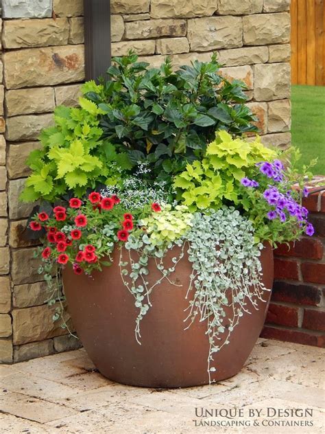 a large potted planter filled with lots of colorful flowers next to a brick wall