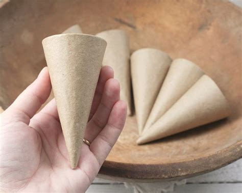 A Person Holding A Cone In Their Hand Next To A Wooden Bowl With Cones On It