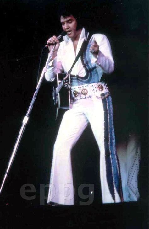 Elvis Presley Performing On Stage In White Pants And Blue Shirt With His Microphone Raised To