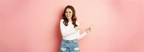 Premium Photo Cute Smiling Brunette Girl Showing Advertisement Pointing Fingers Left At Banner