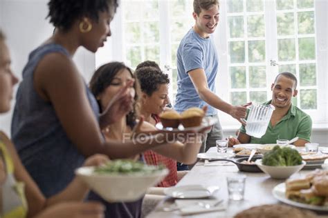 Group Of Men And Women Gathering Around Dining Table And Sharing Meal