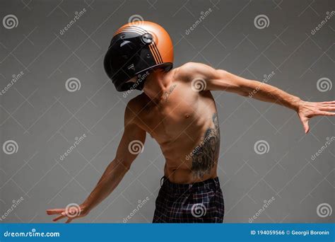 Cool Guy Racer In Helmet With Naked Torso Stands On Gray Background In