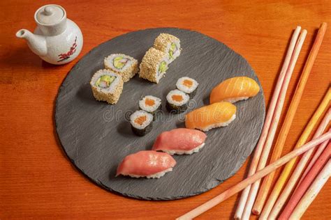 Assorted Sushi On A Circular Black Slate Plate And Sauce Boat With Soy