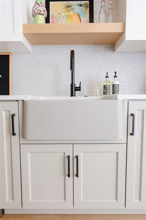 A White Kitchen Sink Sitting Under A Wooden Shelf Next To Cupboards And