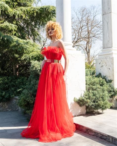 Una Mujer Con Un Vestido Rojo Se Para En Una Acera Frente A Una Columna