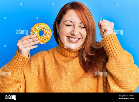 Beautiful Redhead Woman Holding Tasty Colorful Doughnut Screaming Proud Celebrating Victory And