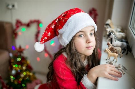 Niñita con un vestido rojo y un sombrero rojo de papá noel mirando a la