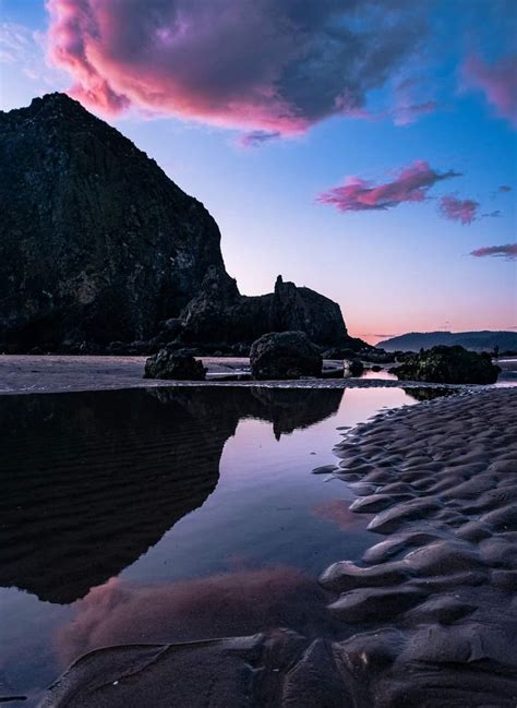 the sky is reflected in the wet sand at low tide beach, with rocks and ...