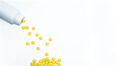 Yellow film coated tablets pills spilling out of pill bottle on white