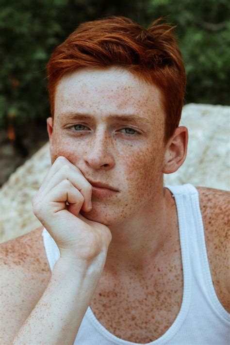 A Young Man With Freckles On His Face Sitting In Front Of A Rock