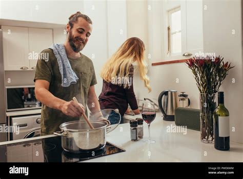 Happy Man Cooking Food While Woman Washing Dishes In Kitchen Couple