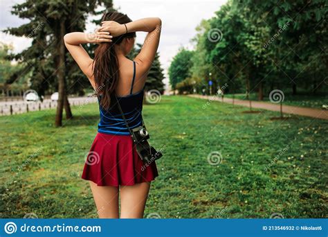 Teen Girl In A Short Skirt Travels With Camera On The Back In Nature On A Sunny Summer Day Stock