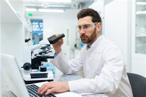 Serious And Thoughtful Scientist Working In Laboratory With Microscope