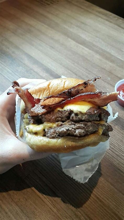 A Person Holding Up A Bacon Cheeseburger On A Bun With Some Ketchup