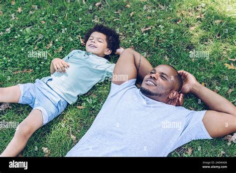 Smiling African American Father And Son Lying On Lawn While Resting In