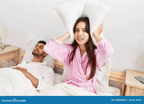 Woman Covering Ears With Pillow Irritated For Snore Lying In Bed At