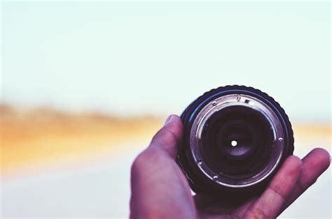 Premium Photo Cropped Hand Holding Camera Lens At Beach Against Sky