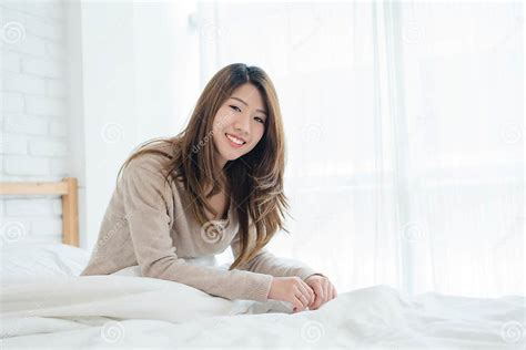 Happy Beautiful Young Asian Woman Waking Up In Morning Sitting On Bed Stretching In Cozy