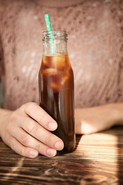 Mujer sosteniendo una botella de café frío en la mesa de madera Foto