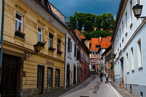 Two People Walking Down An Alley Way Between Old Buildings With Windows