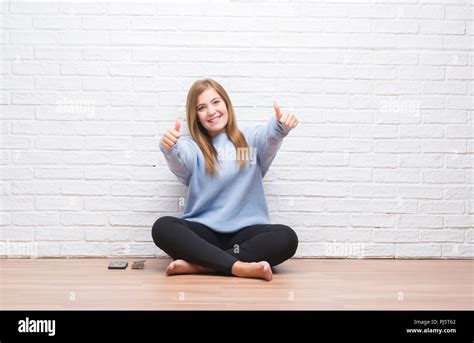 Young Adult Woman Sitting On The Floor In Autumn Over White Brick Wall