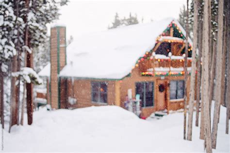 A Cabin Surrounded By Deep Snow And Pine Trees With Falling Snow And