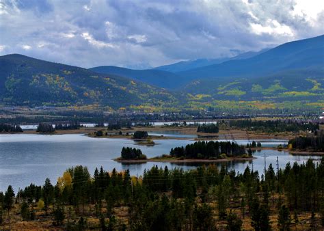 a lake surrounded by trees and mountains under cloudy skies