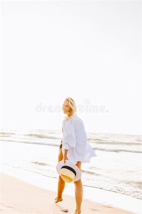 Beautiful Blonde Slim Woman Wearing Black Bikini And White Shirt Walk On Beach Of Sea Or Ocean