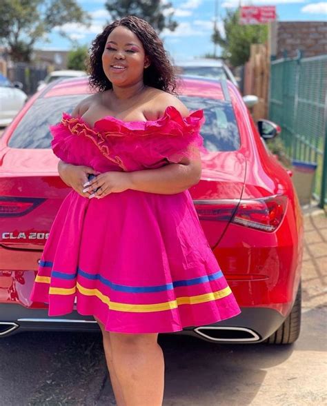 A Woman In A Pink Dress Standing Next To A Red Car With Her Hands On