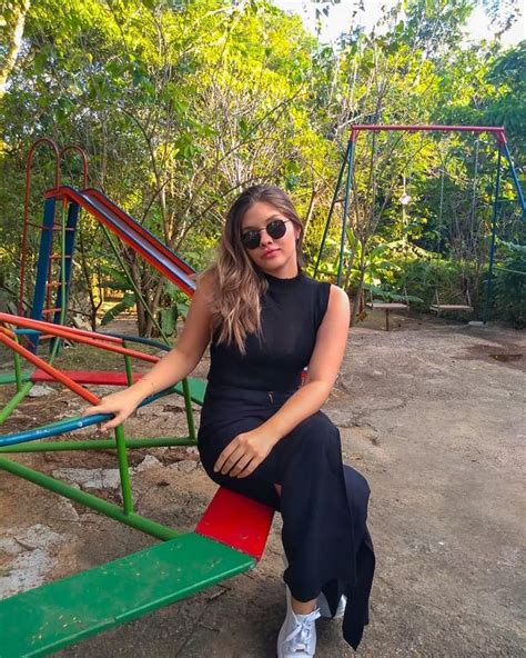 A Woman Sitting On Top Of A Green Bench Next To A Swing Set And Trees