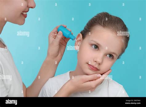 Mother Dripping Medication Into Daughters Ear On Light Blue Background