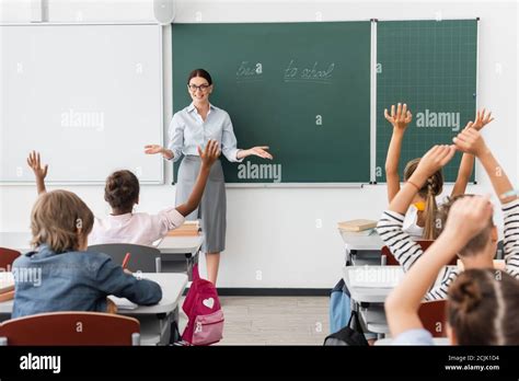 Back View Of Multiethnic Pupils With Hands In Air And Teacher Standing