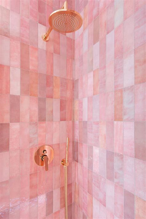 A Pink Tiled Shower With Gold Faucet And Hand Held Shower Head In The