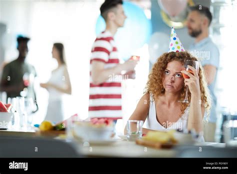 Bored Girl With Glass Of Drink Sitting By Table At Birthday Party While Her Friends