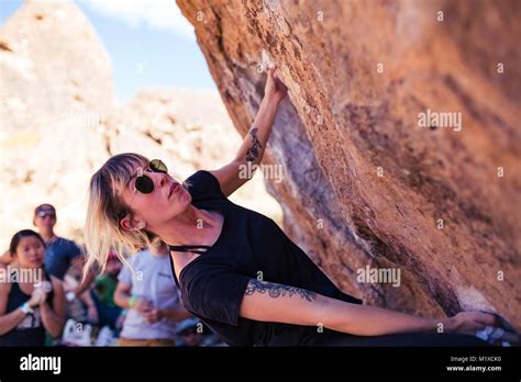 Dünne blonde kaukasische Frau mit Arm tattoos Rock klettert auf Felsbrocken in der Wüste von