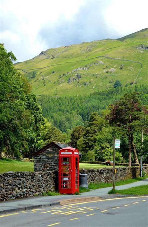 A Red Phone Booth Sitting On The Side Of A Road Next To A Lush Green