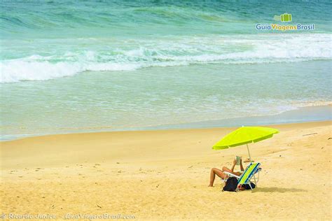 Imagem de uma pessoa lendo embaixo guarda sol verde limão e ao fundo o