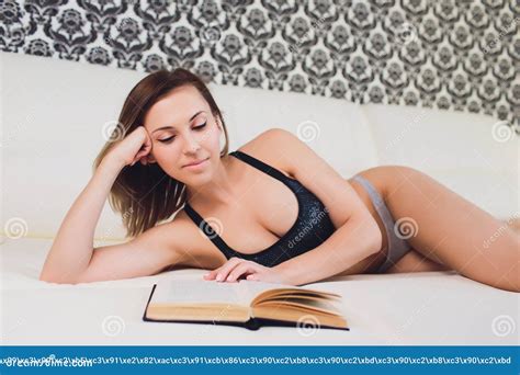 Woman Lying On A Sofa While Reading A Book In A Living Room Stock