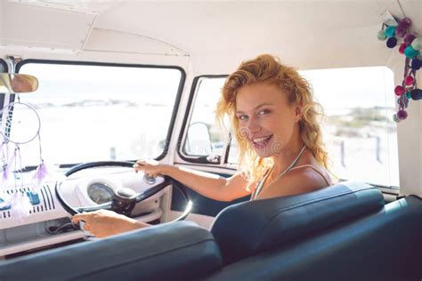 Woman Looking At Camera While Driving A Camper Van At Beach Stock Photo