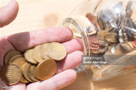 A Person Hold Coins In The Hand Close To A Glass Jar With Many Coins