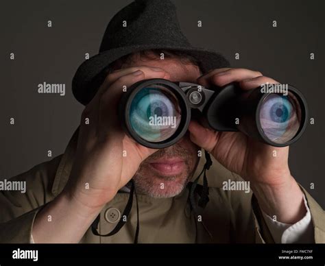 Photograph Of A Man In Trench Coat And Hat Looking Through Binoculars With Huge Cartoonish Eyes