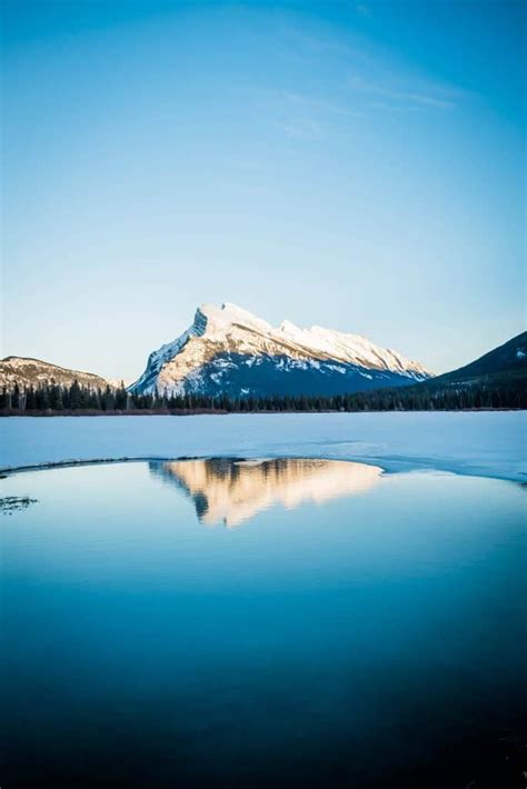 The Mountains Are Covered In Snow And Reflected In The Still Water On