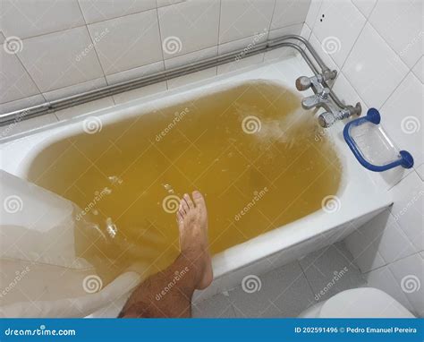 Bathtub Full Of Yellow Water Due To Rust Or Impurities With Human Leg